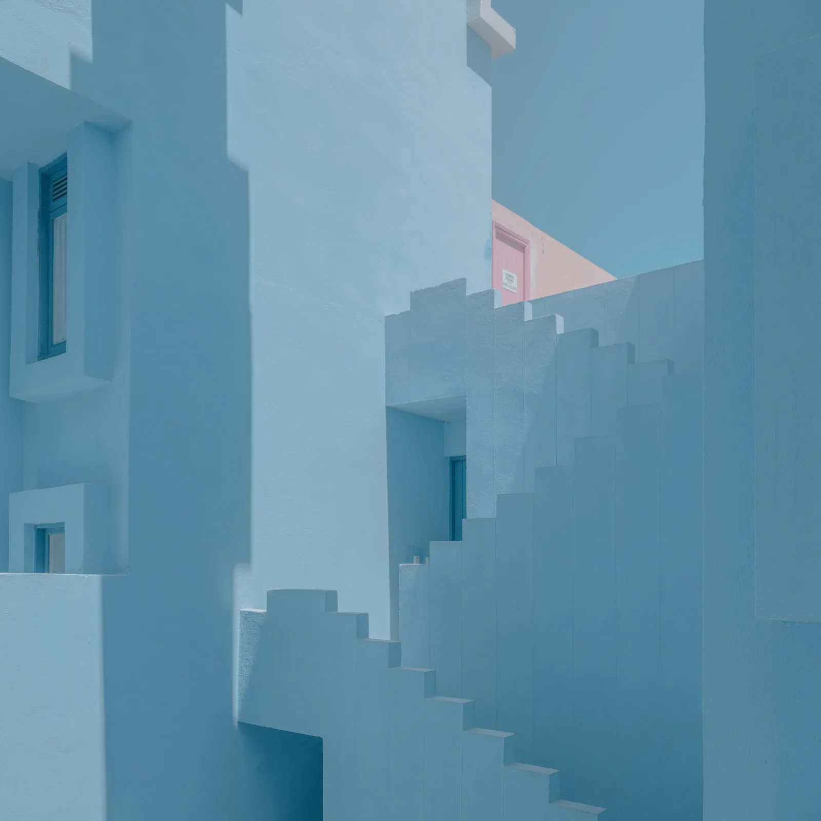 Quiet, stepped architecture and a pink door in a blue building — limited edition fine art print by Ludwig Favre Quiet, stepped architecture and a pink door in a blue building — limited edition fine art print by Ludwig Favre