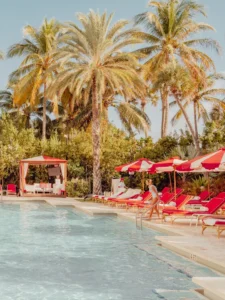 A serene Miami Beach swimming pool scene with red umbrellas, fine art print by Ludwig Favre