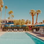 Tranquil Palm Springs pool scene with blue umbrellas and palm trees — limited edition fine art print by Ludwig Favre