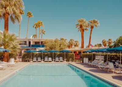 Tranquil Palm Springs pool scene with blue umbrellas and palm trees — limited edition fine art print by Ludwig Favre