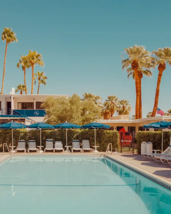 Tranquil Palm Springs pool scene with blue umbrellas and palm trees — limited edition fine art print by Ludwig Favre