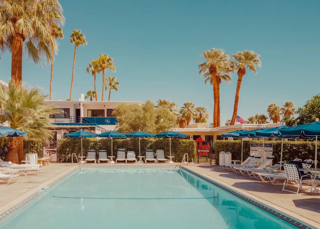 Tranquil swimming pool scene in Palm Springs, bathed in warm light — limited edition fine art print by Ludwig Favre Tranquil Palm Springs pool scene with blue umbrellas and palm trees — limited edition fine art print by Ludwig Favre