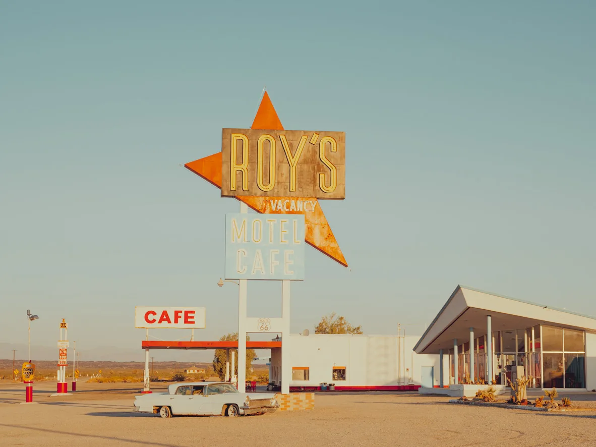 Vintage motel sign and cafe along a desert highway — limited edition fine art print by Ludwig Favre Vintage Roy's Motel 2 sign and classic car in the Mojave Desert landscape — limited edition fine art print by Ludwig Favre