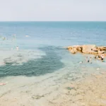 Swimmers around rocky outcrops in clear Mediterranean waters under soft summer light, limited edition fine art print by Ludwig Favre