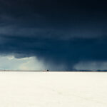 Dark storm clouds loom over Bonneville Salt Flats in Utah, contrasting sharply with distant mountains under moody lighting.