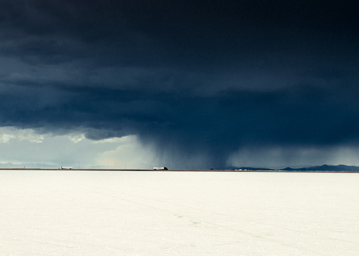 Dark storm clouds loom over Bonneville Salt Flats in Utah, contrasting sharply with distant mountains under moody lighting.