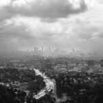 Black and white view of downtown Los Angeles with a winding highway cutting through the city, seen from the Hollywood Hills under an overcast sky.