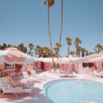 Retro pink motel swimming pool scene in Palm Springs, California with lounge chairs, umbrellas, and palm trees, limited edition fine art print by Ludwig Favre