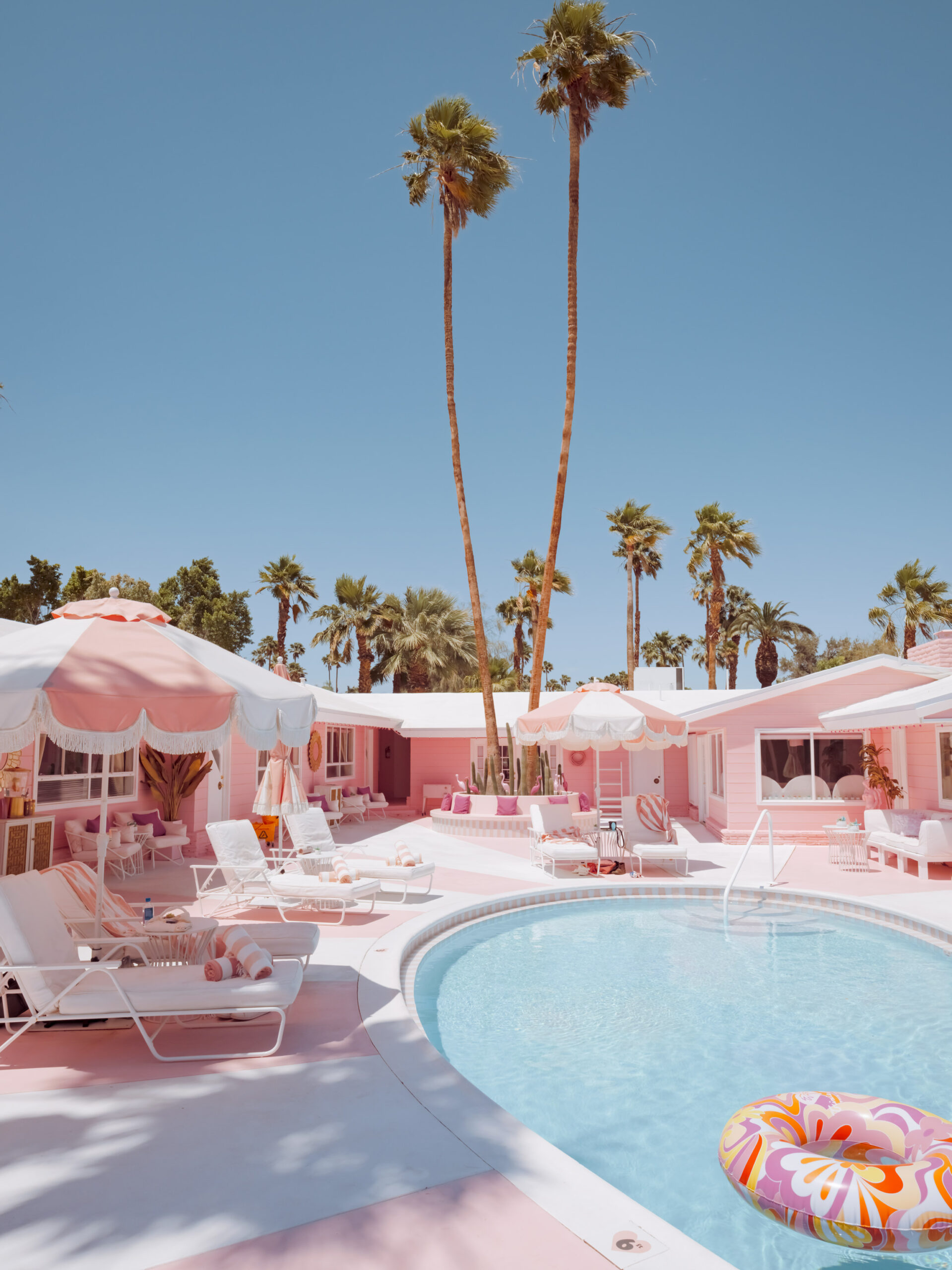 Retro pink motel swimming pool scene in Palm Springs, California with lounge chairs, umbrellas, and palm trees, limited edition fine art print by Ludwig Favre