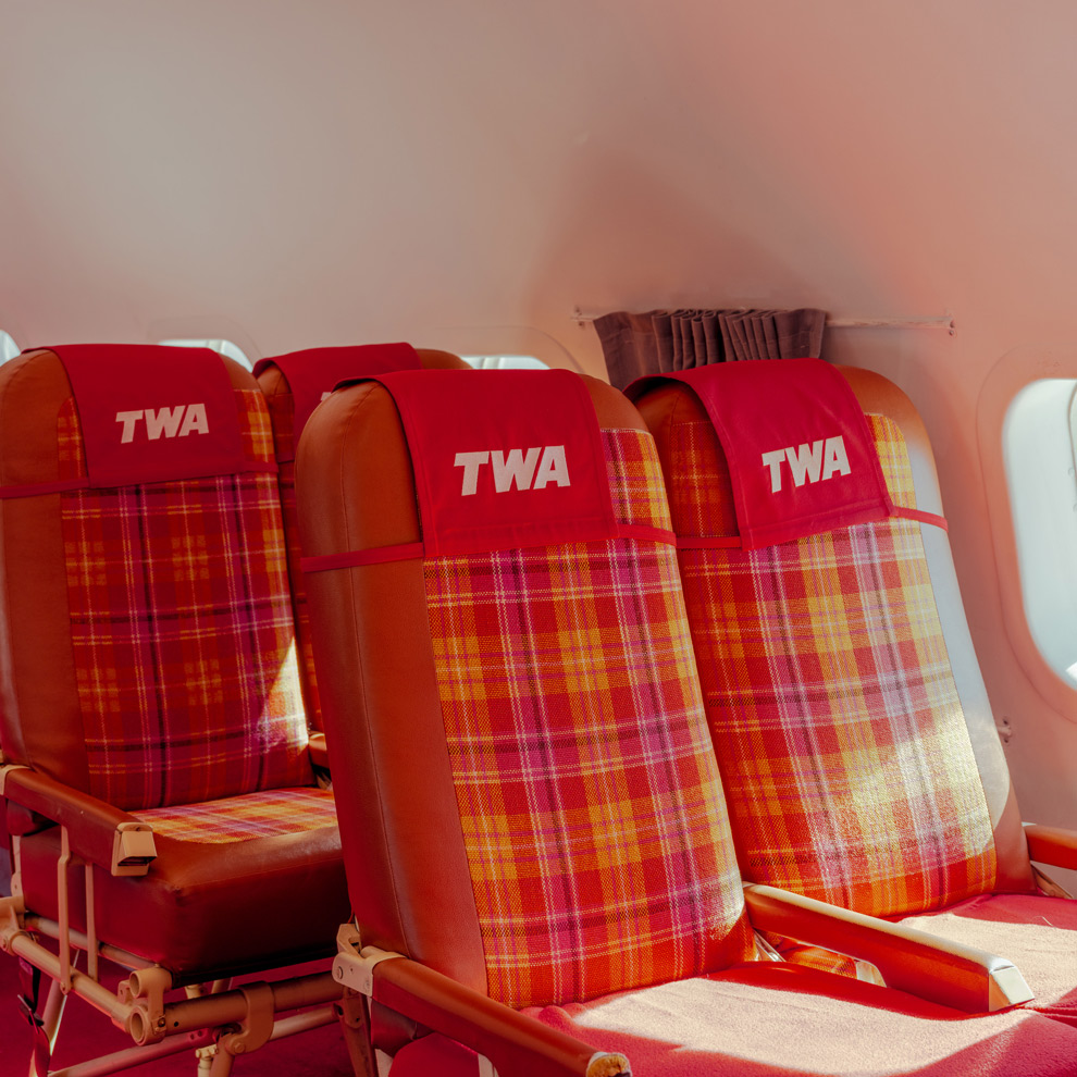 Red plaid TWA airline seats beside a cabin window, limited edition fine art photograph by Ludwig Favre