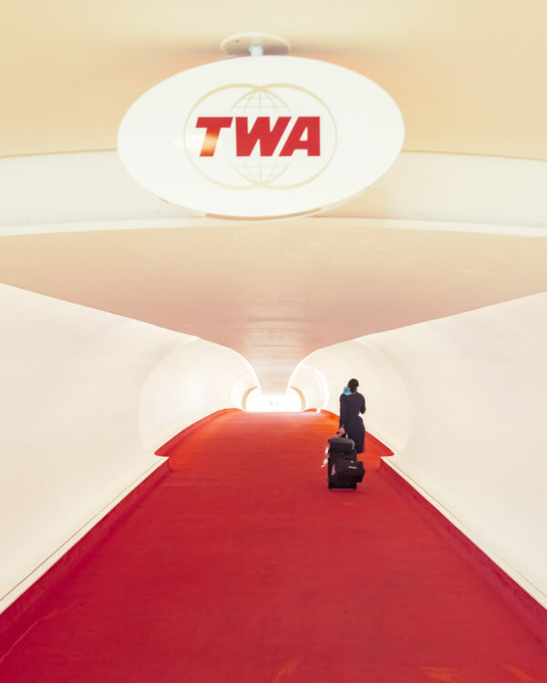TWA Hotel red carpet flight tube with a lone traveler under the oval TWA sign, JFK Airport, limited edition fine art photograph by Ludwig Favre