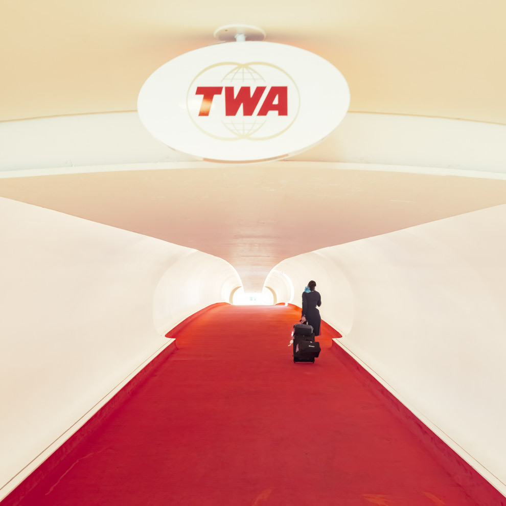 TWA Hotel red carpet flight tube with a lone traveler under the oval TWA sign, JFK Airport, limited edition fine art photograph by Ludwig Favre