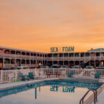 Turquoise swimming pool reflecting teal Sea Foam Motel sign under an orange sky in the Outer Banks, fine art print by Ludwig Favre