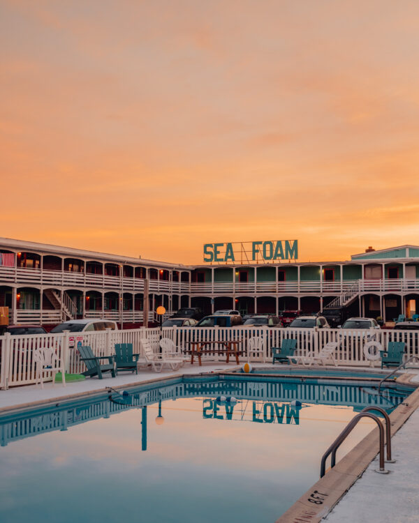 Turquoise swimming pool reflecting teal Sea Foam Motel sign under an orange sky in the Outer Banks, fine art print by Ludwig Favre