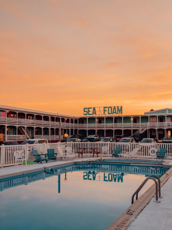 Turquoise swimming pool reflecting teal Sea Foam Motel sign under an orange sky in the Outer Banks, fine art print by Ludwig Favre