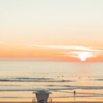 A lifeguard tower numbered 5 on a sandy beach at sunset, with ocean waves under a glowing orange sky.