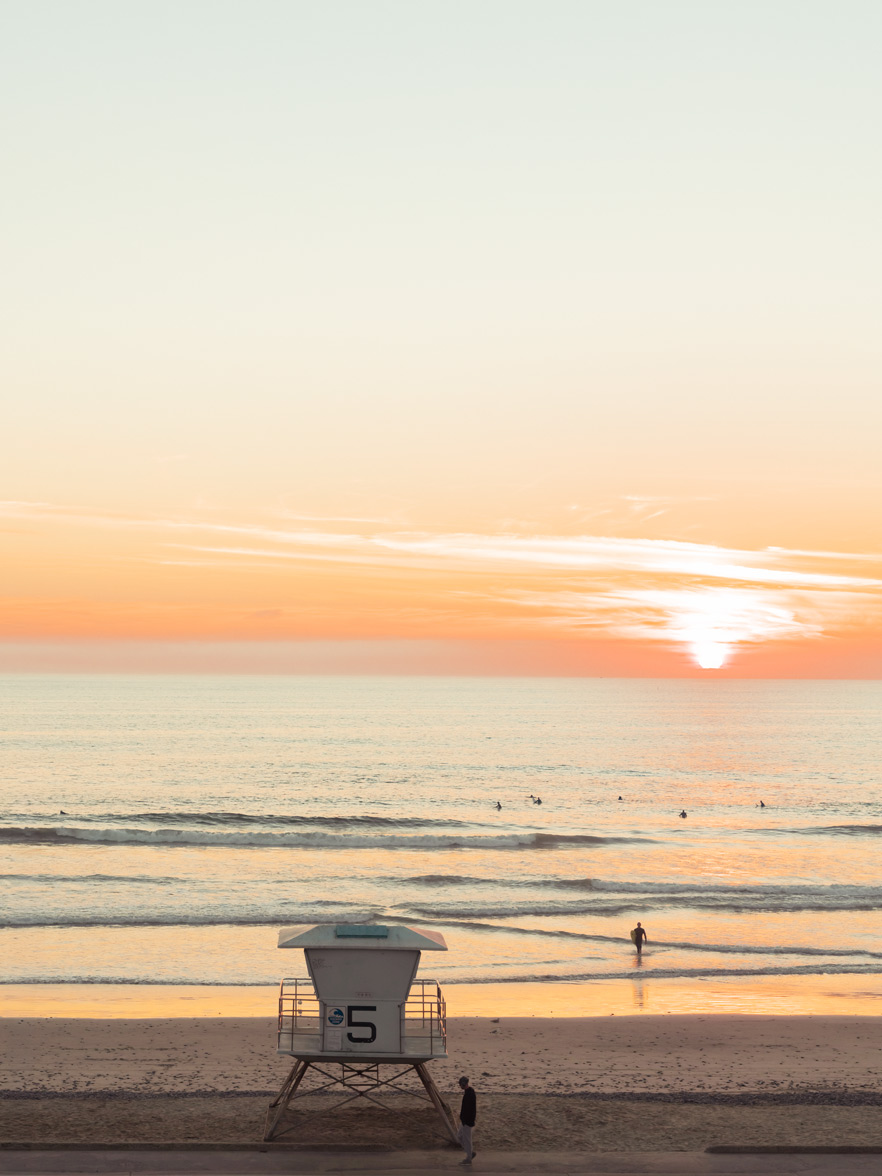 A lifeguard tower numbered 5 on a sandy beach at sunset, with ocean waves under a glowing orange sky. A lifeguard tower numbered 5 on a sandy beach at sunset, with ocean waves under a glowing orange sky.